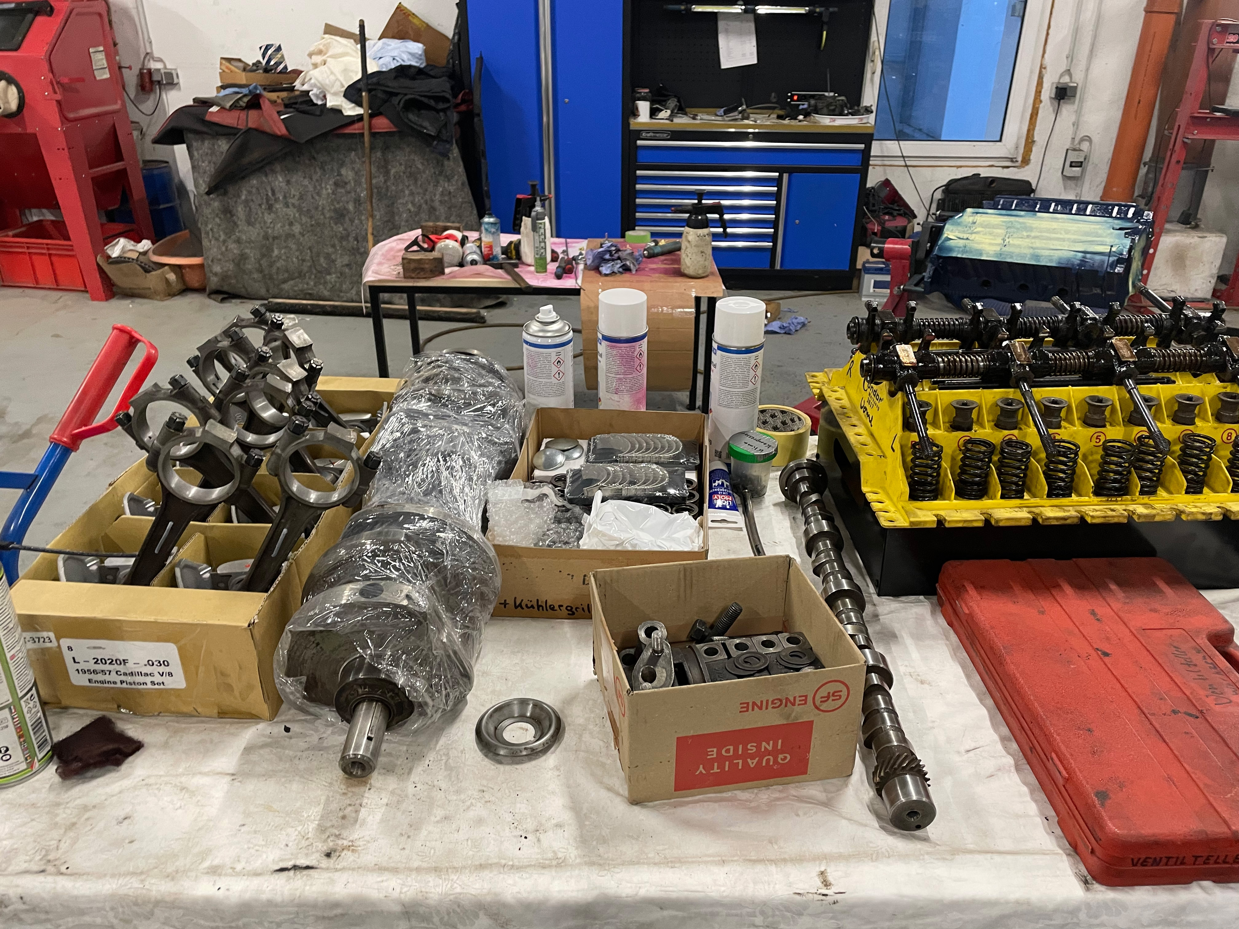 Arbeitsplatz in der Oldtimer Profi Werkstatt mit Motorteilen für klassische US-Fahrzeuge (Cadillac, Lincoln 1956-1979), darunter Kolben, Kurbelwelle, Nockenwelle und Ventilfedern.