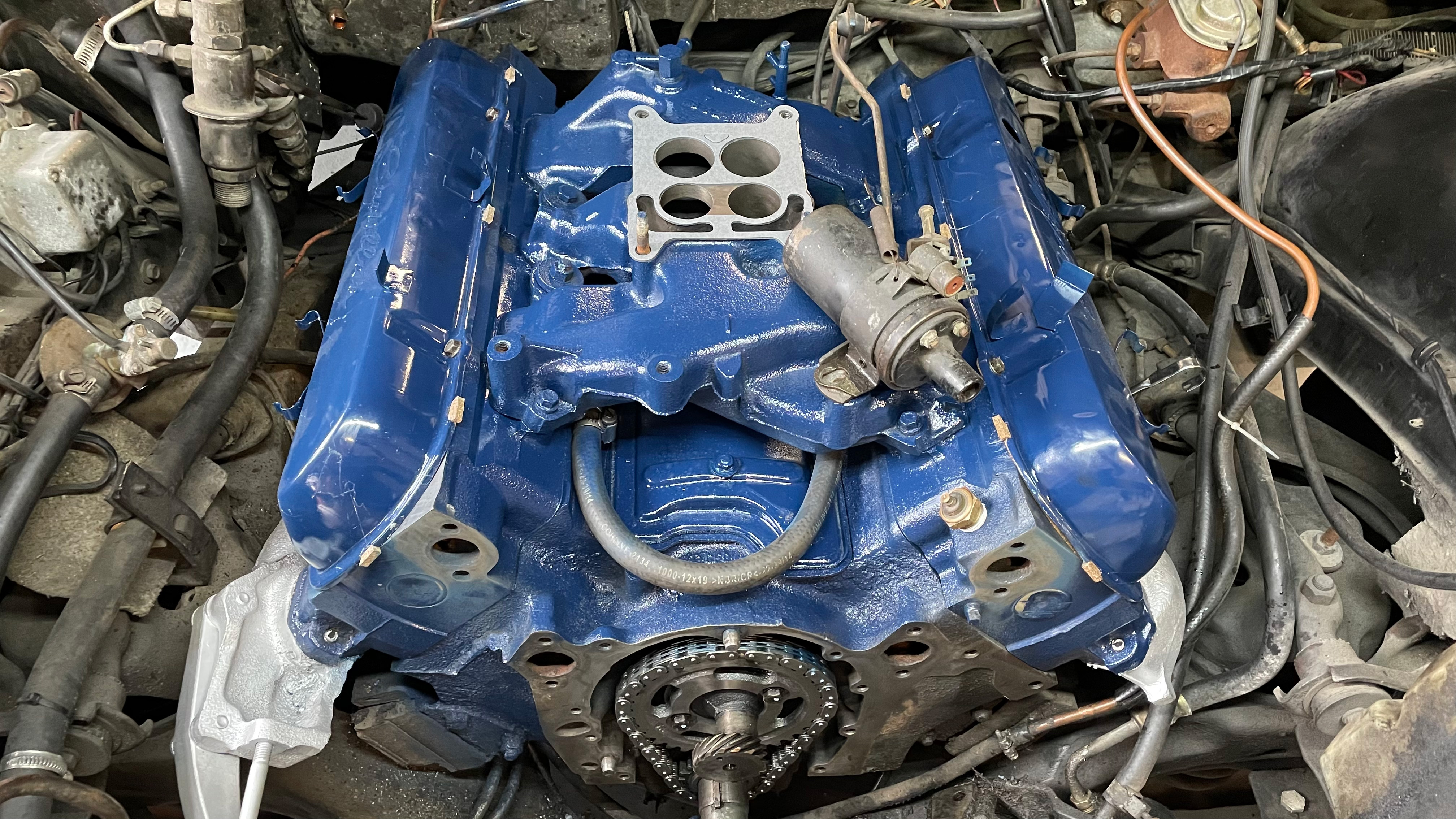 Blaue Motorbaugruppe eines klassischen US-Fahrzeugs (z. B. Cadillac oder Lincoln) im Reparaturprozess, mit sichtbaren Komponenten wie Anlasser und Zündverteiler – typisch für die fachgerechte Instandsetzung bei Oldtimer Profi.