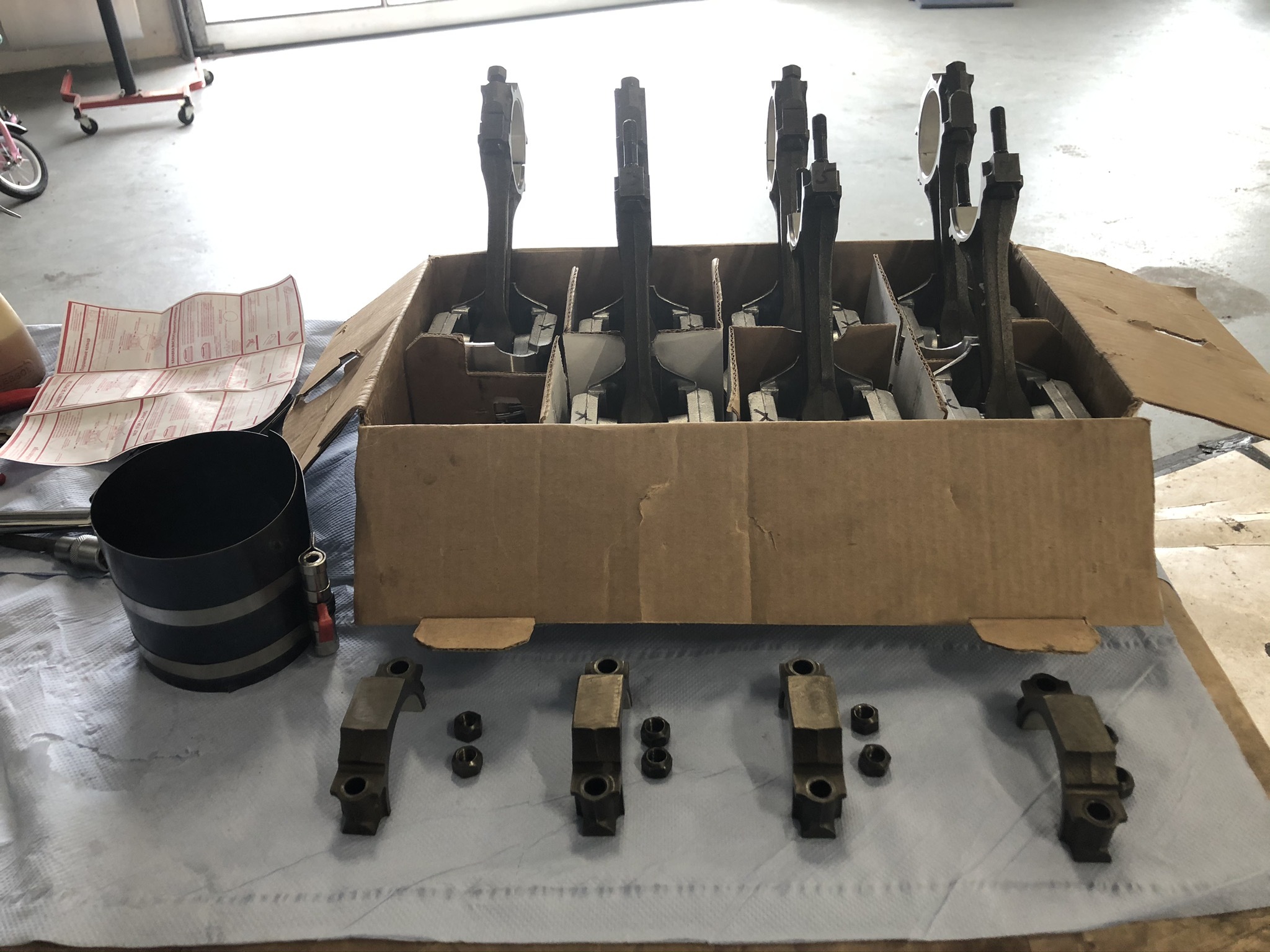 Kolbenstangen und weitere Motorteile für klassische US-Fahrzeuge (z. B. Cadillac, Lincoln) in einer Kartonbox und auf einem Tuch ausgelegt – typisch für Reparaturarbeiten in einer Oldtimer-Werkstatt.