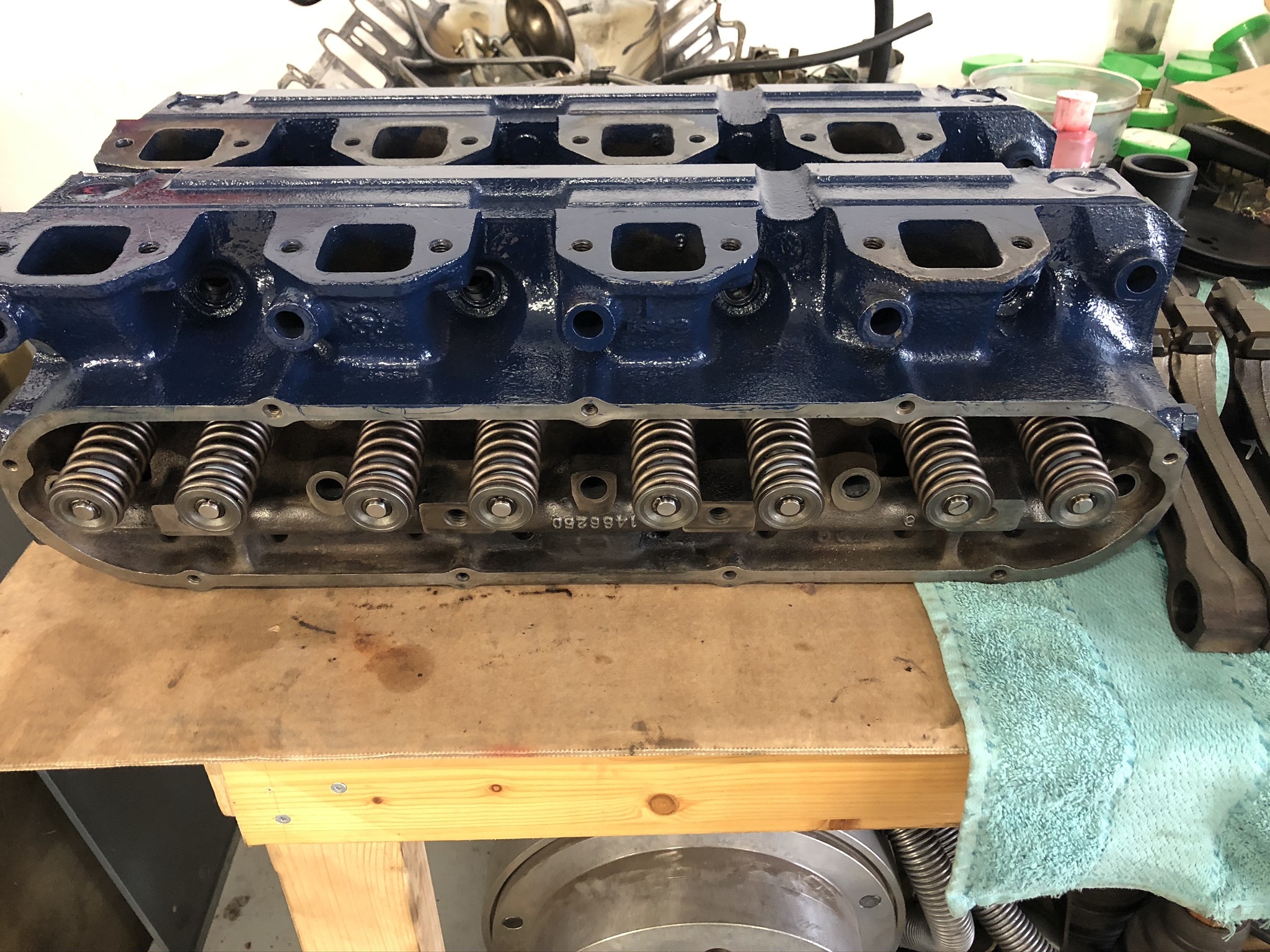 Blau lackierter Zylinderkopf mit Ventilfedern auf einer Werkbank – typisches Ersatzteil für die Reparatur klassischer US-Fahrzeuge in der Oldtimer Profi Werkstatt.