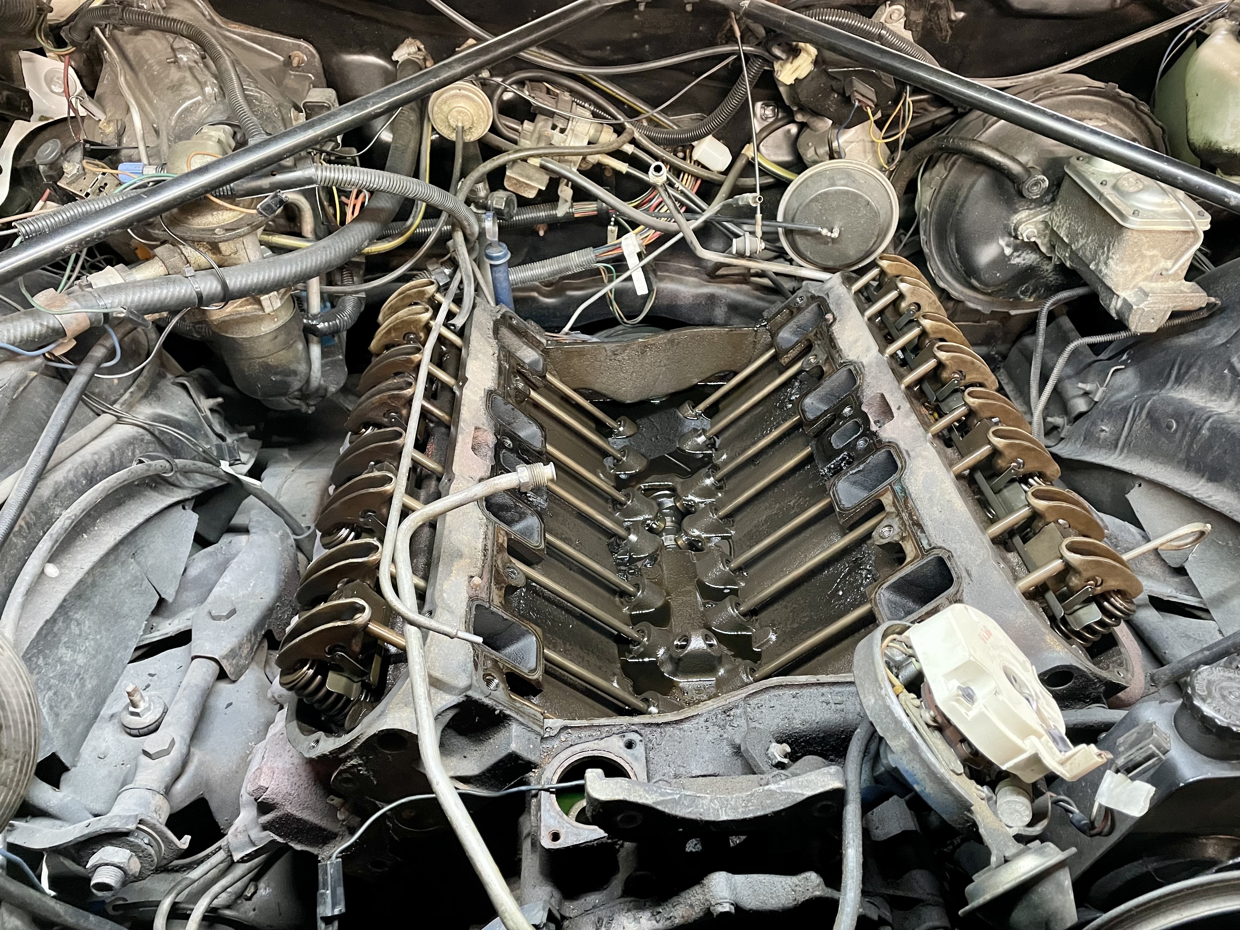 Motorraum eines klassischen US-Fahrzeugs mit entfernten Ventildeckeln, zeigend die Ventilmechanik – typisch für Oldtimer-Reparaturen und Wartung.
