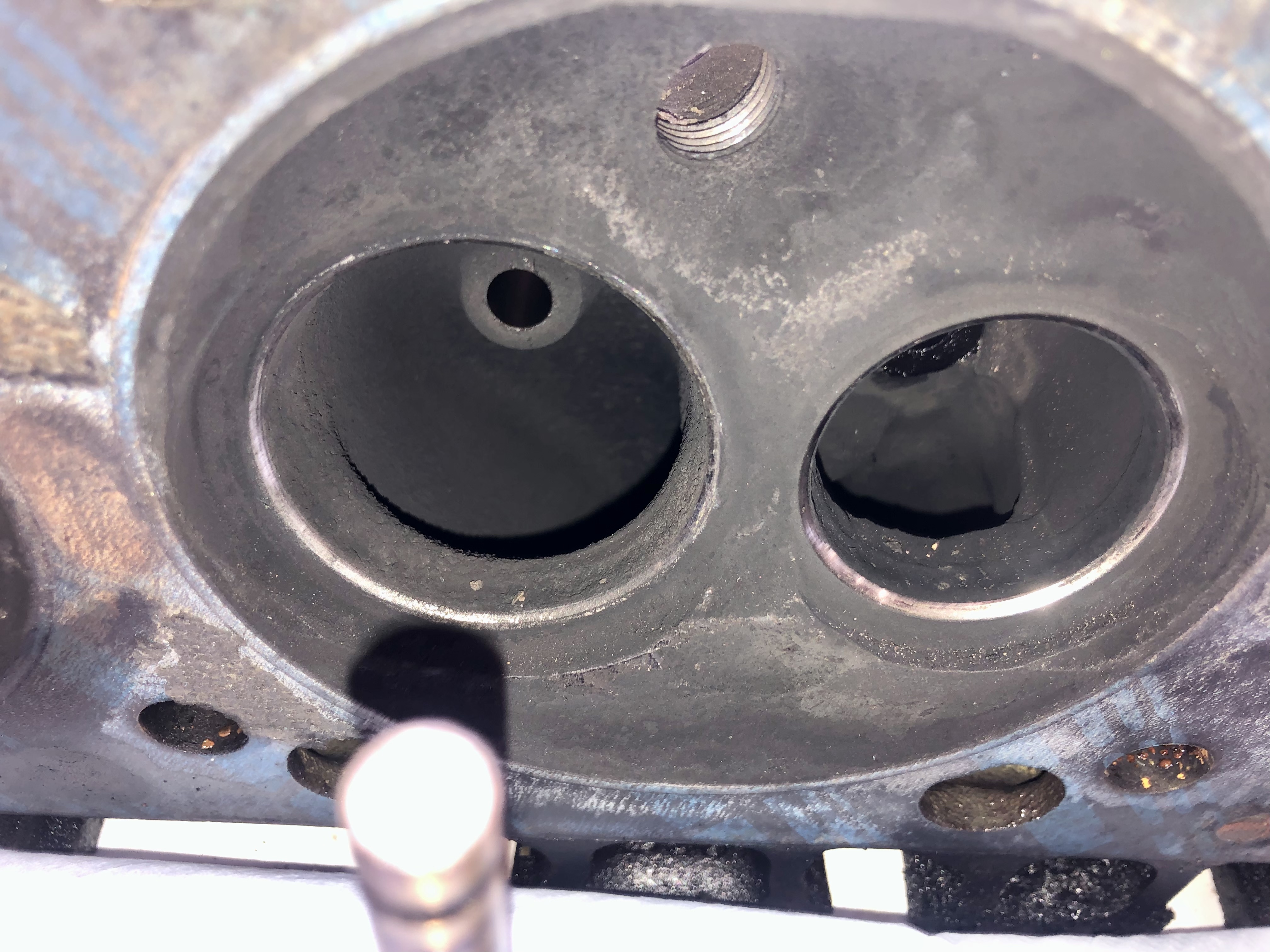 Nahaufnahme eines abgenutzten Motorbauteils (vermutlich Zylinderkopf) mit zwei runden Öffnungen und einem Gewindebolzen, typisch für klassische US-Fahrzeuge wie Cadillac oder Lincoln (Baujahre 1956-1979), die in der spezialisierten Werkstatt Oldtimer Profi repariert und gewartet werden.