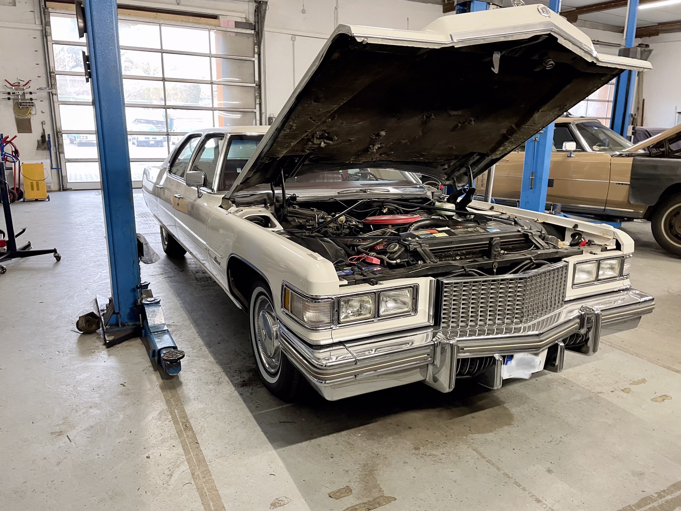 Weißer klassischer Cadillac mit geöffneter Motorhaube in einer Werkstatt für Oldtimer – spezialisiert auf US-Fahrzeuge wie Cadillac und Lincoln der Baujahre 1956 bis 1979.