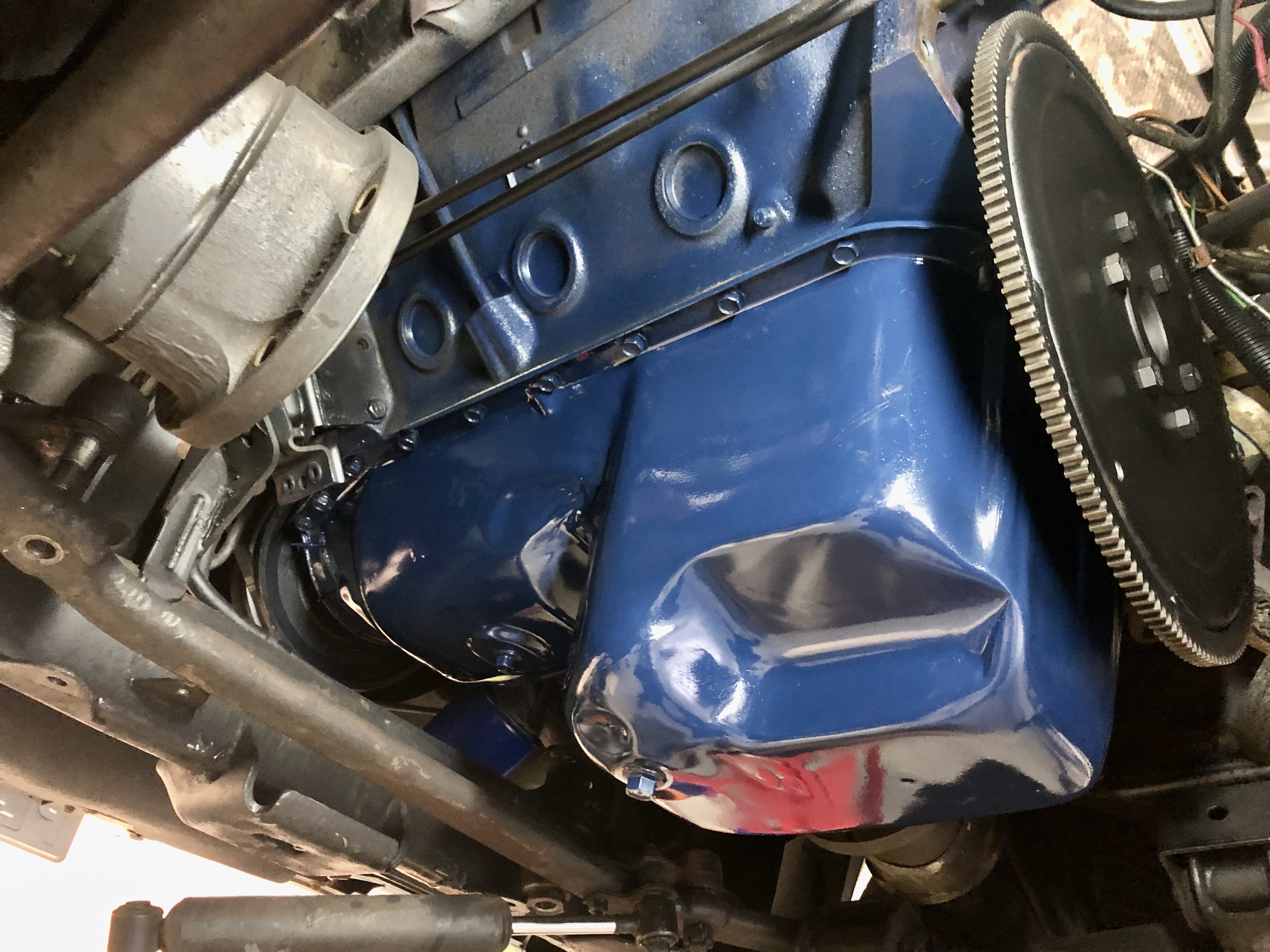 Blaue, lackierte Motor- oder Getriebekomponente eines klassischen US-Fahrzeugs (z.B. Cadillac/Lincoln 1956-1979) mit umgebenden mechanischen Teilen wie dem Schwungrad, typisch für die Restauration in einer spezialisierten Oldtimer-Werkstatt.