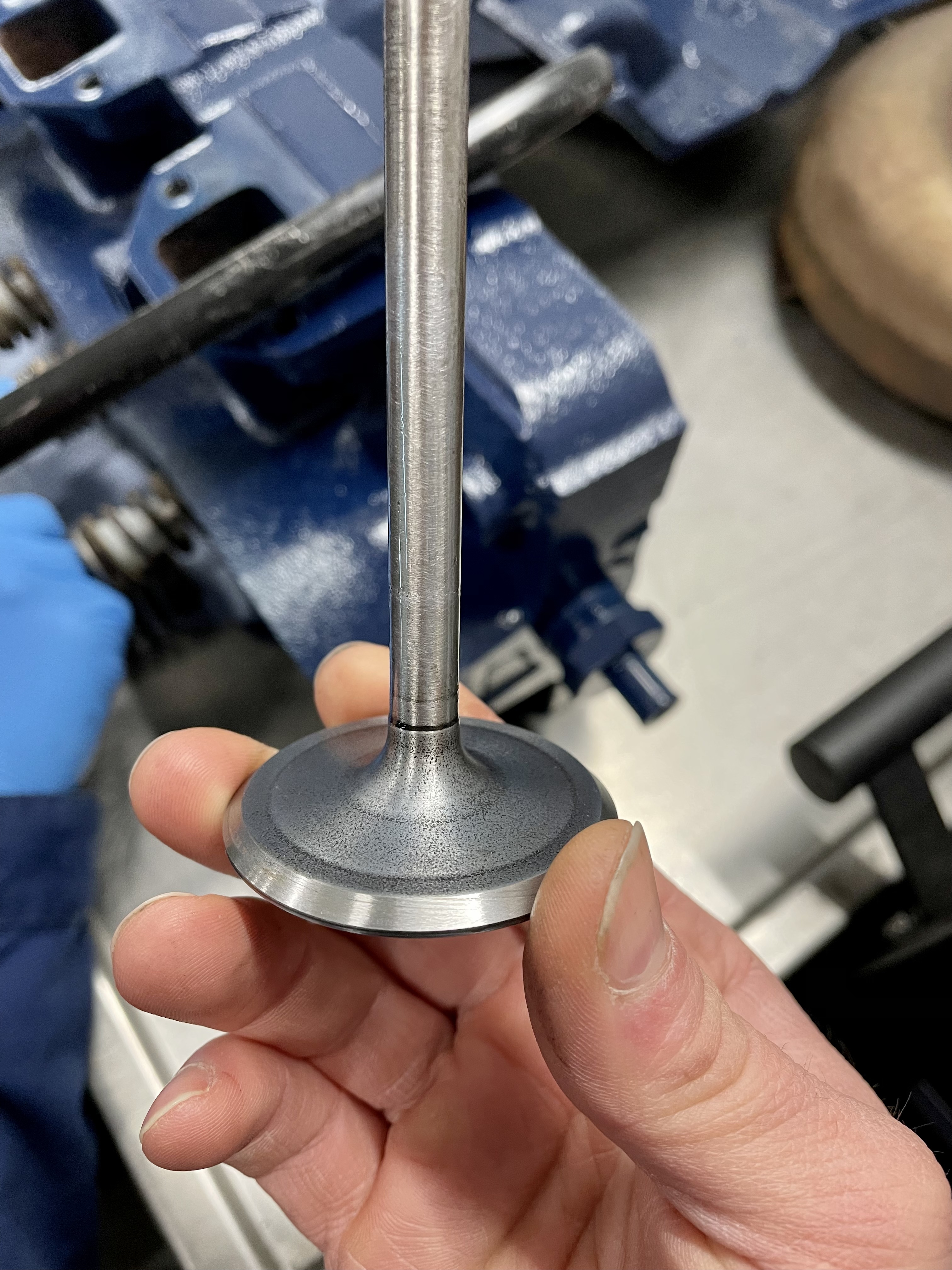 Hand hält ein Metall-Zylinderkopfventil, typisch für die Reparatur klassischer US-Fahrzeuge (Cadillac, Lincoln 1956-1979) in der Oldtimer Profi Werkstatt.