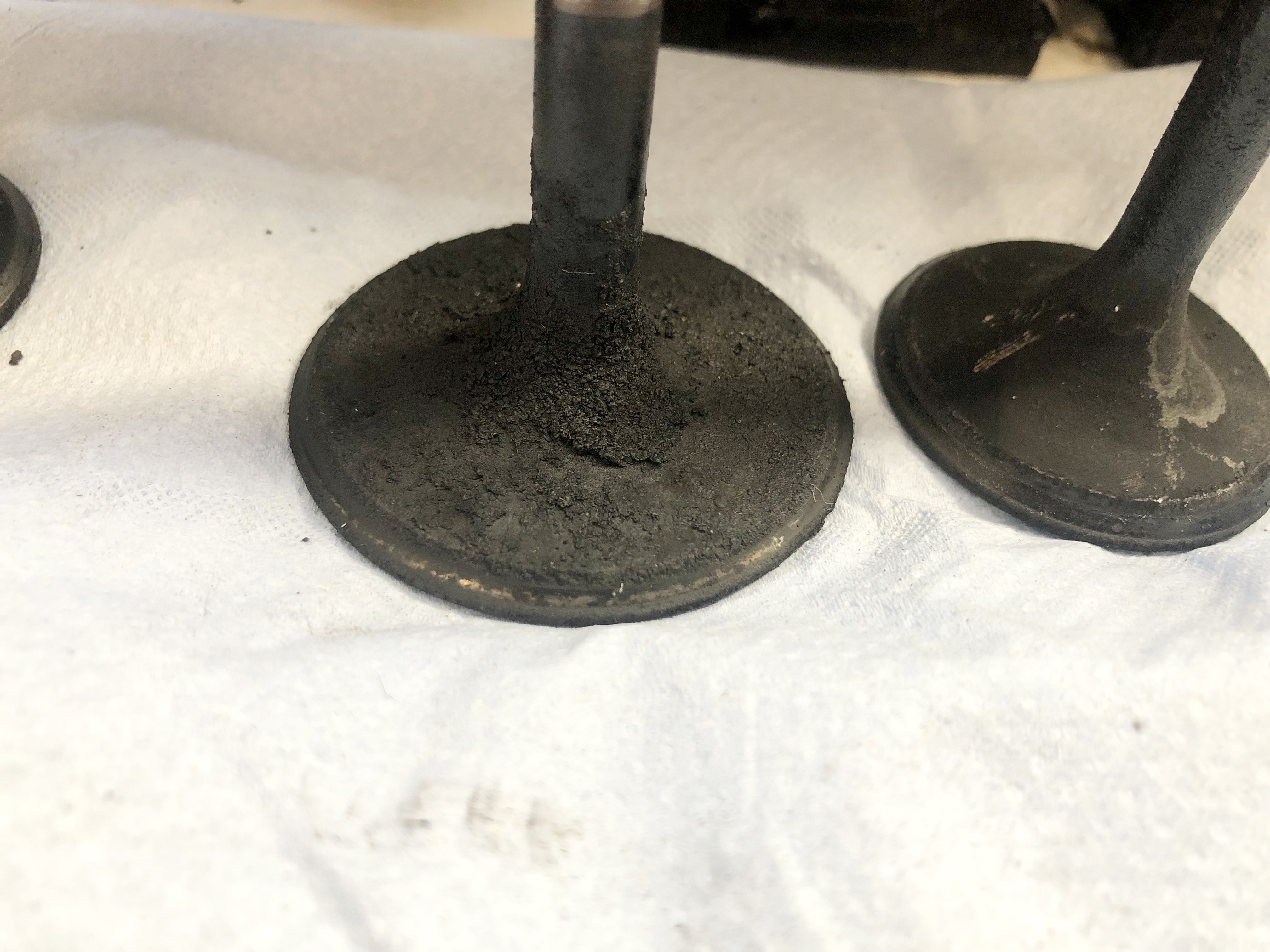 Zwei verschmutzte Ventilstiele von klassischen US-Fahrzeugen (z. B. Cadillac, Lincoln) mit Kohlenstoffablagerungen – typisch für den Service in einer spezialisierten Oldtimer-Werkstatt.
