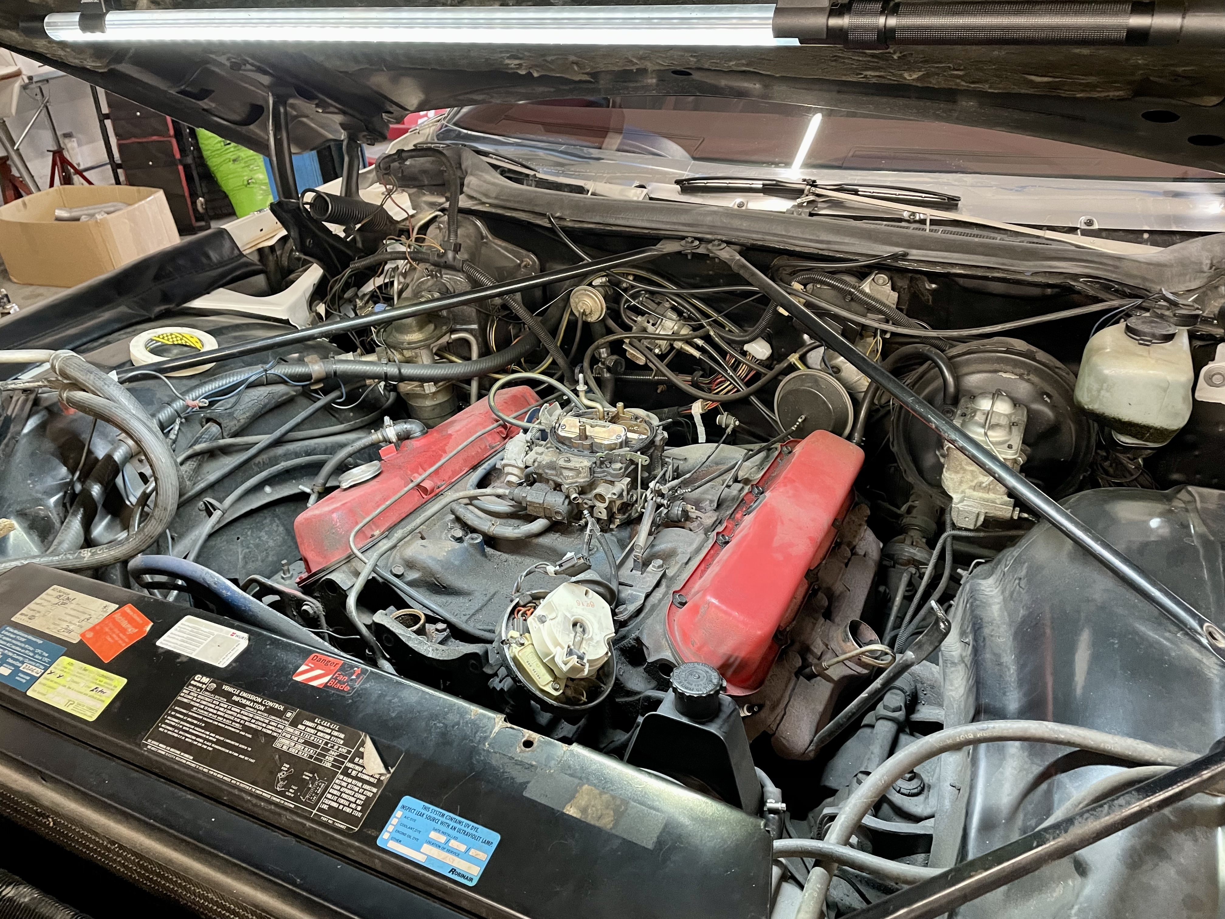 Motorraum eines klassischen US-Fahrzeugs (vermutlich Cadillac oder Lincoln, Baujahr 1956–1979) mit roten Zylinderkopfdeckeln, Vergaser und veralteter Verkabelung – typisch für die fachgerechte Reparatur und Wartung in der Oldtimer Profi Werkstatt.